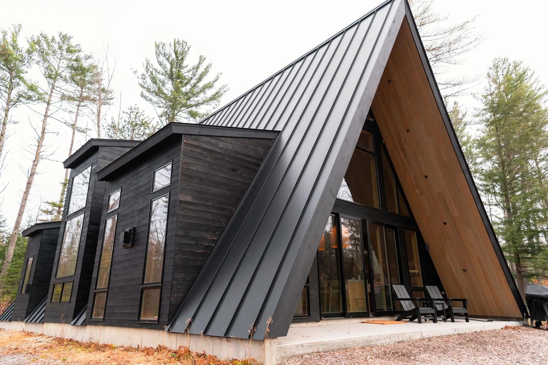 A modern black A-frame cabin with a standing-seam metal roof