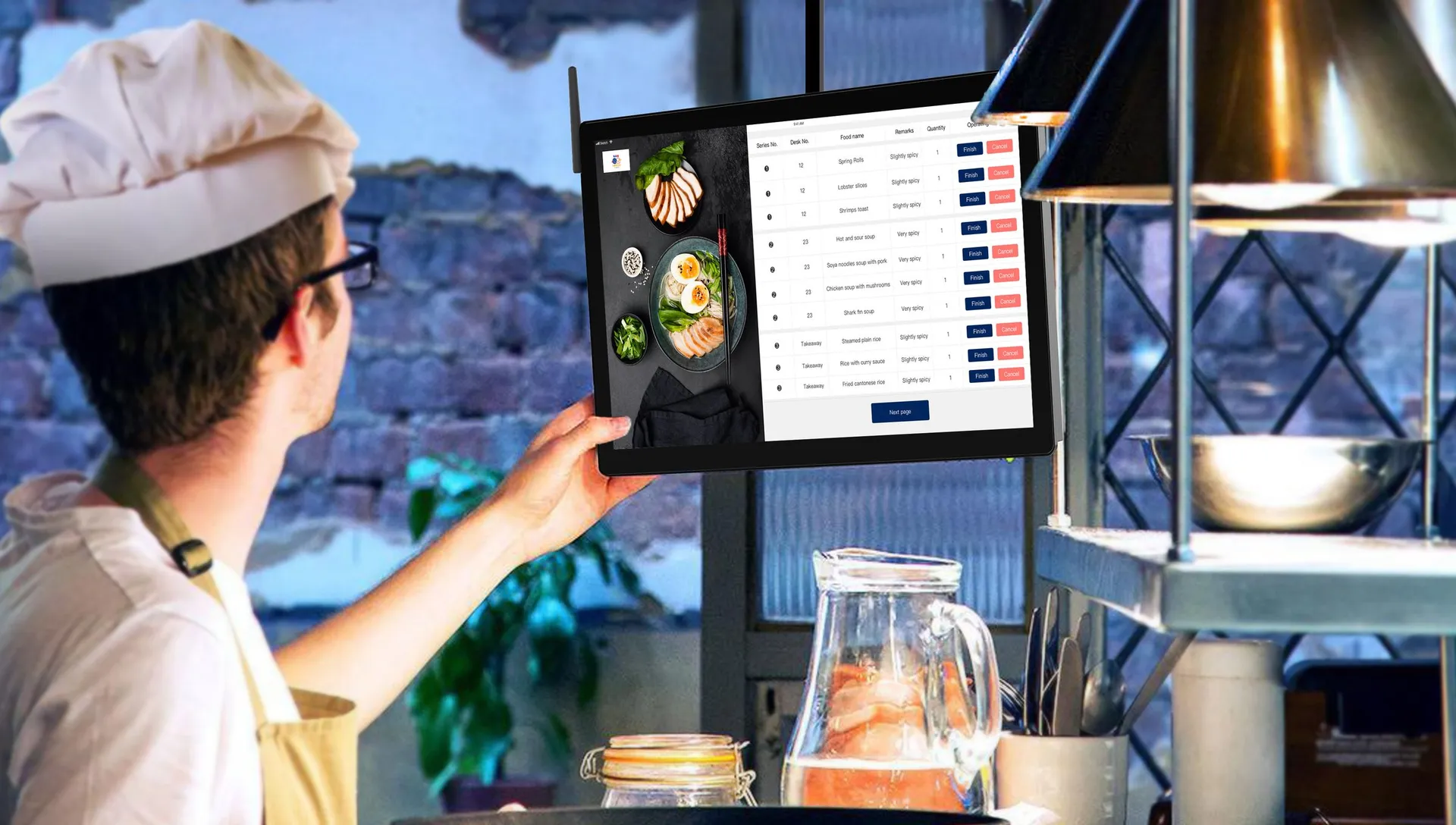a cook in a white hat reaching up to a wall-mounted order screen in a restaurant kitchen
