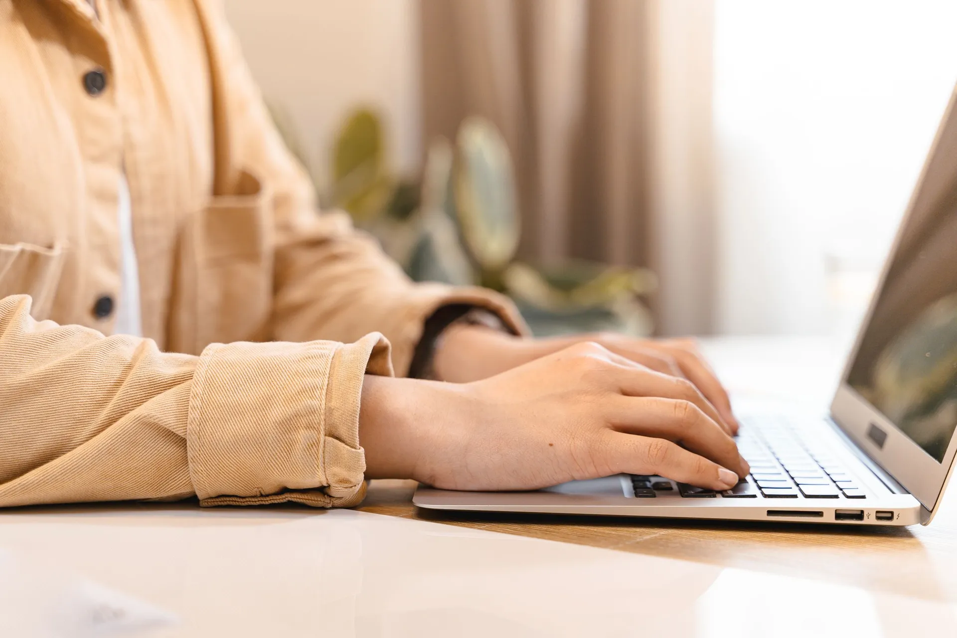 close-up of hands typing on a laptop on a light wooden desk