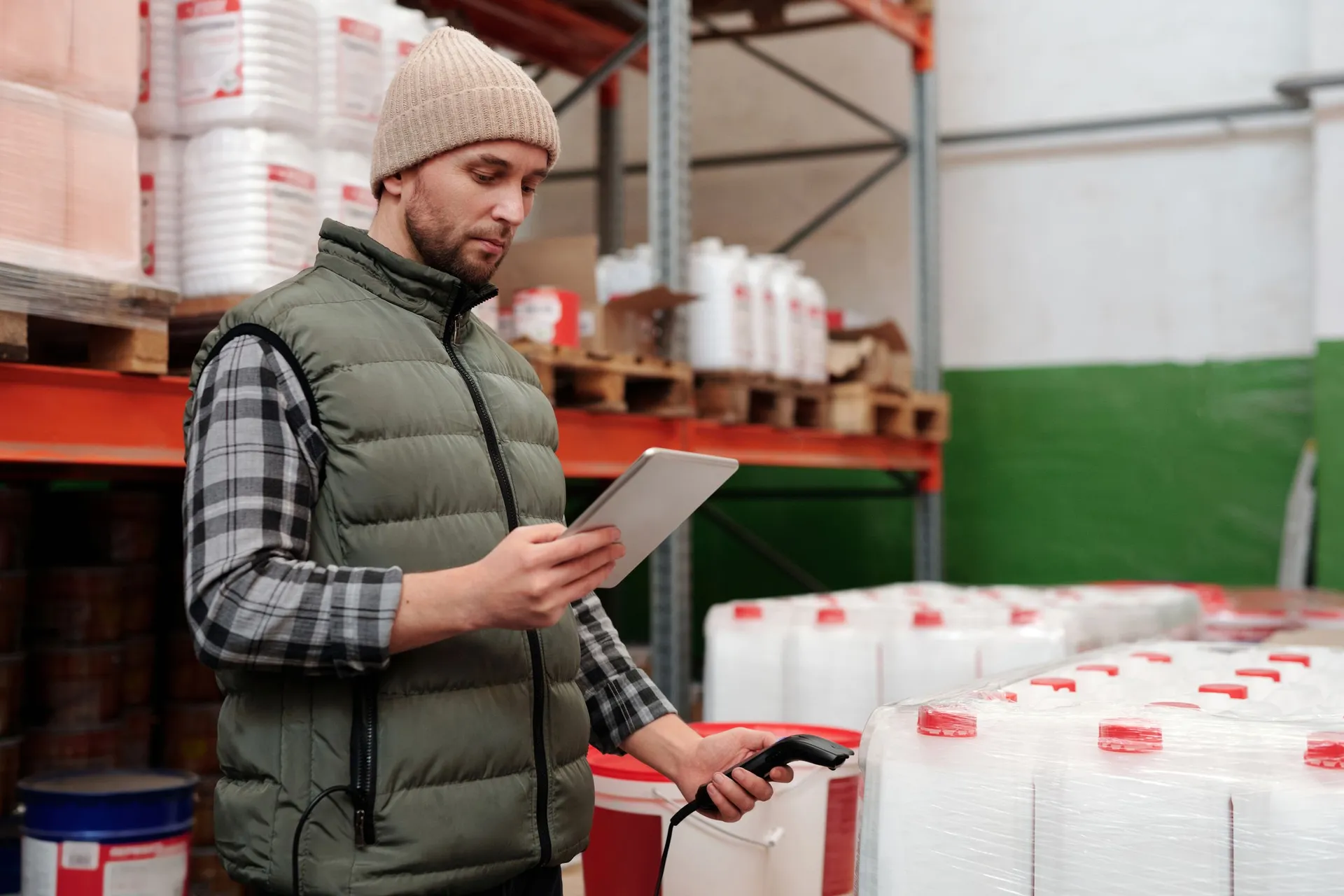 a worker holding a tablet and a handheld scanner between warehouse shelves