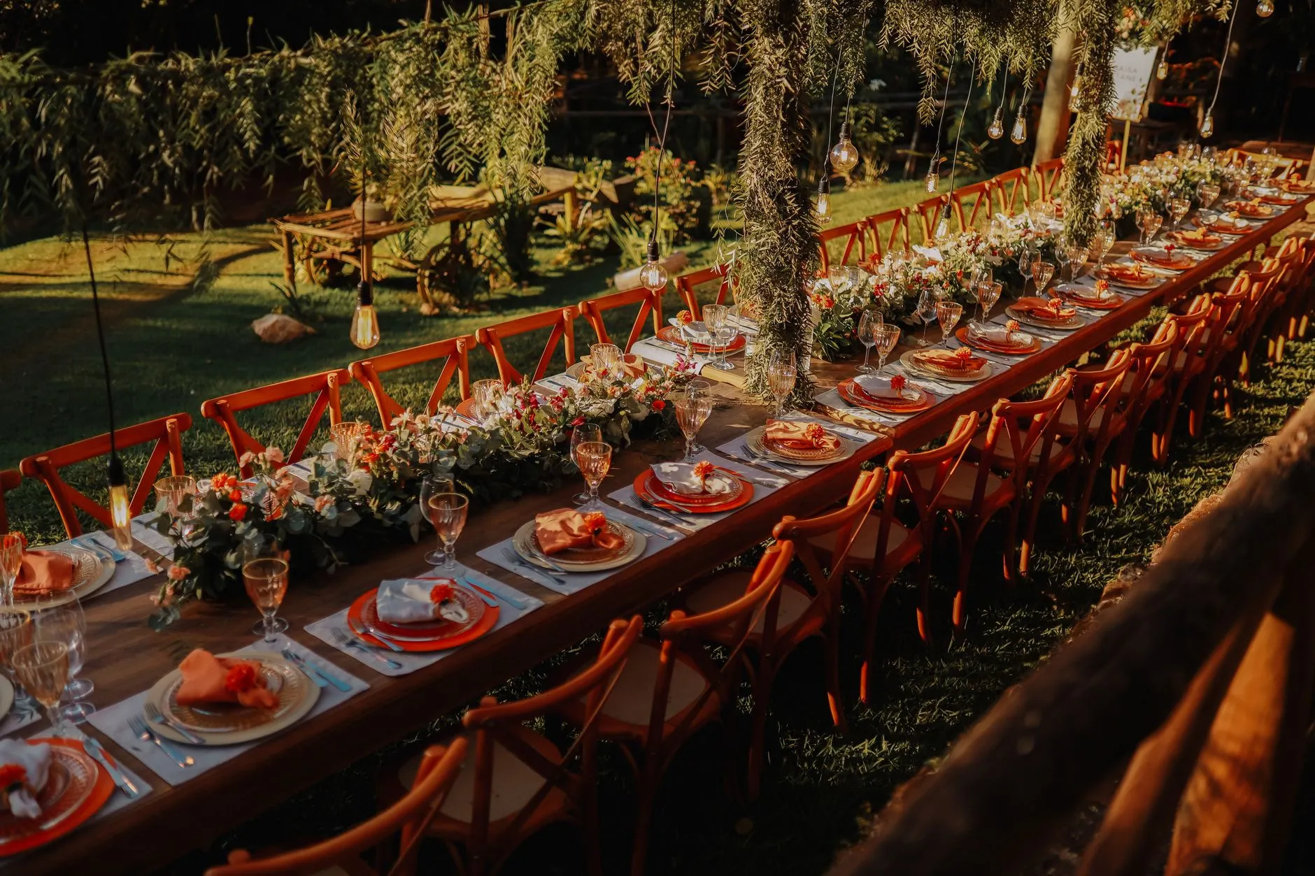 a long celebration table with red chairs set in a garden