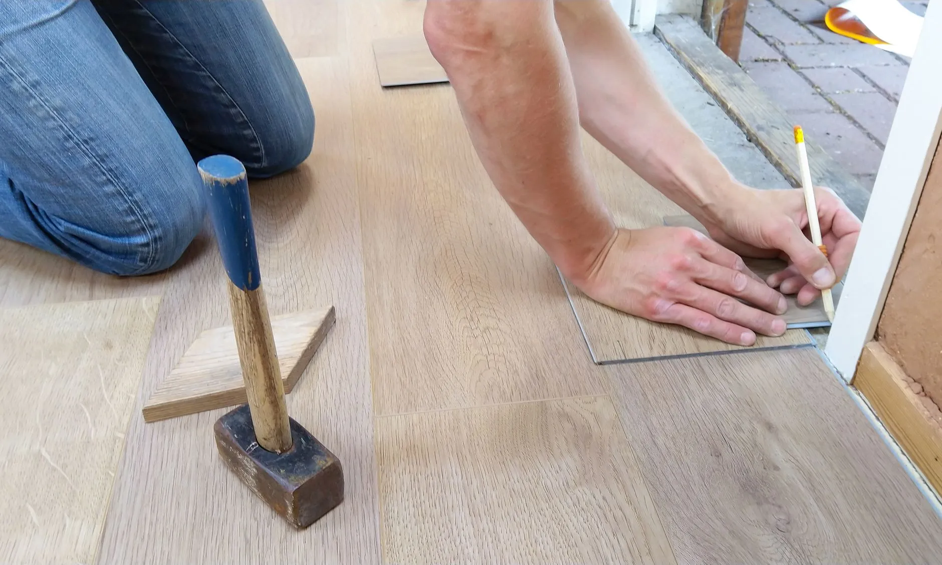 an installer marking a light laminate plank with a pencil beside a mallet