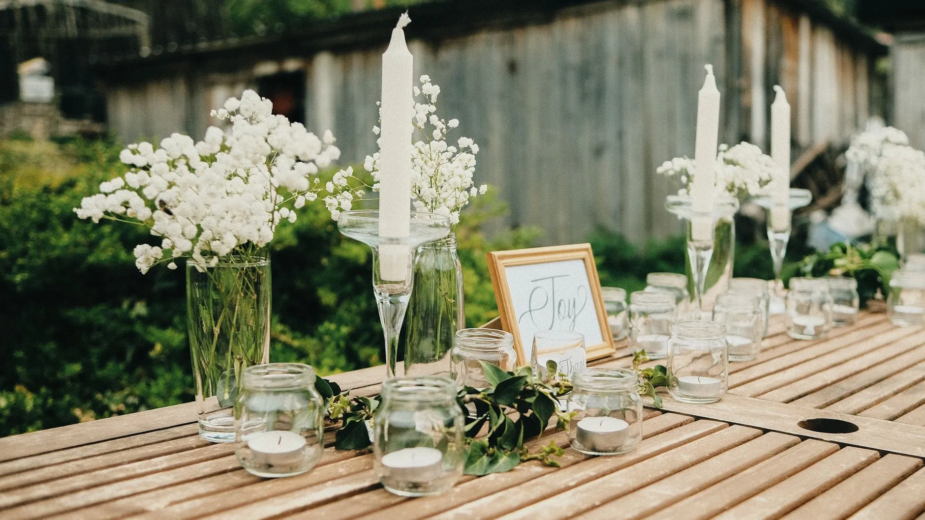 an outdoor wooden table with baby's breath in jars and taper candles