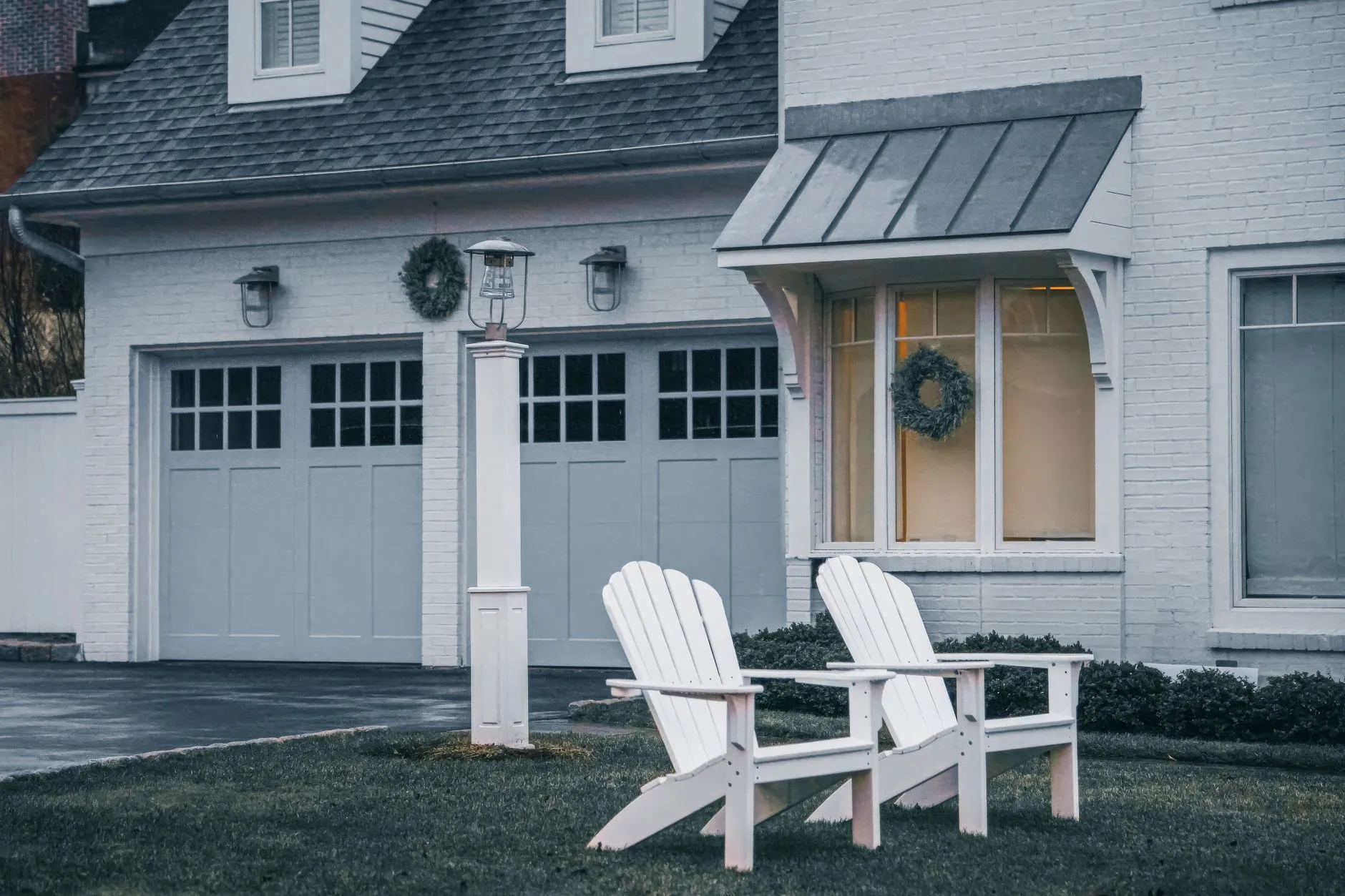 white carriage-style garage doors with window lites beside two Adirondack chairs