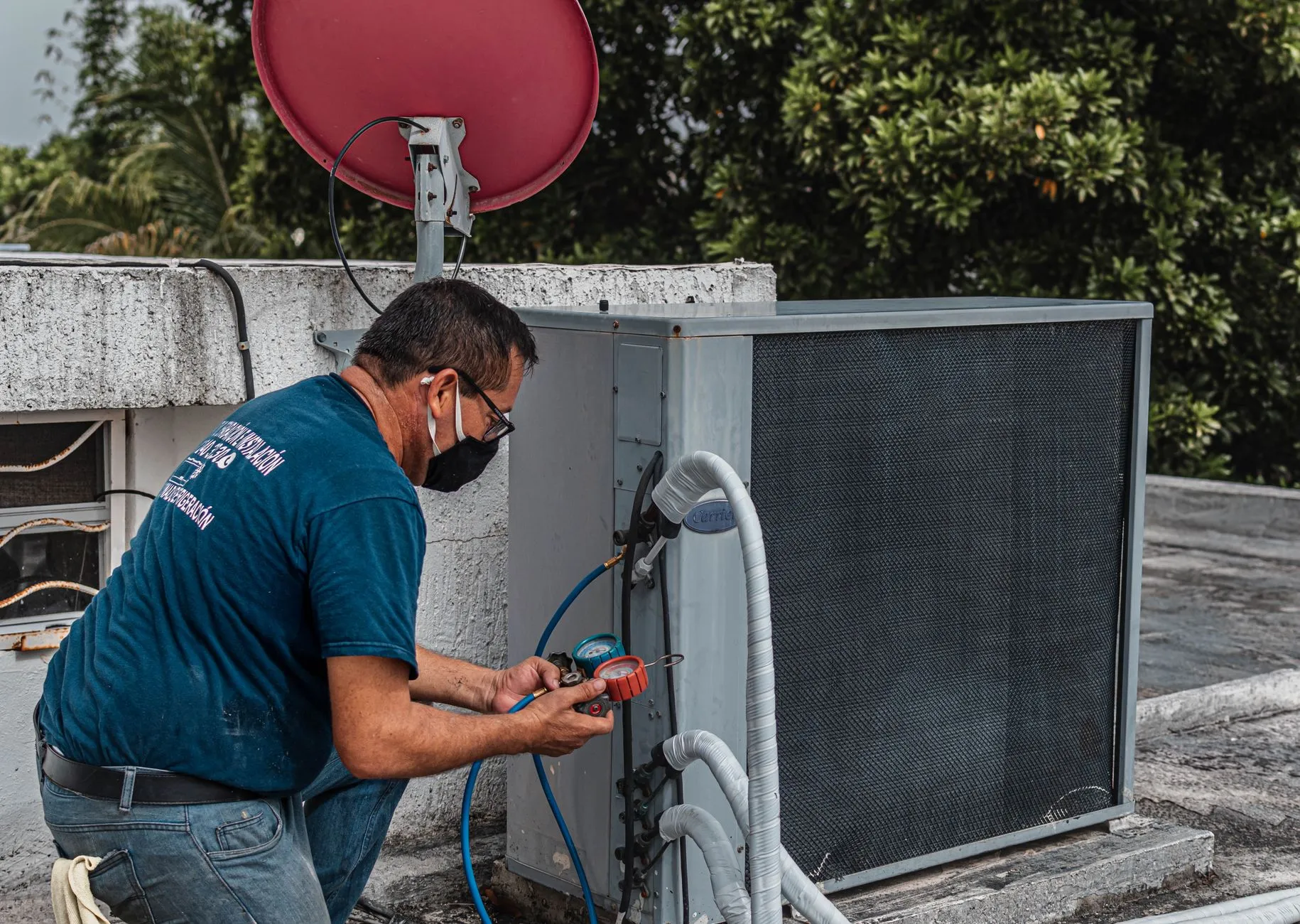 HVAC technician with refrigerant gauges at an AC unit