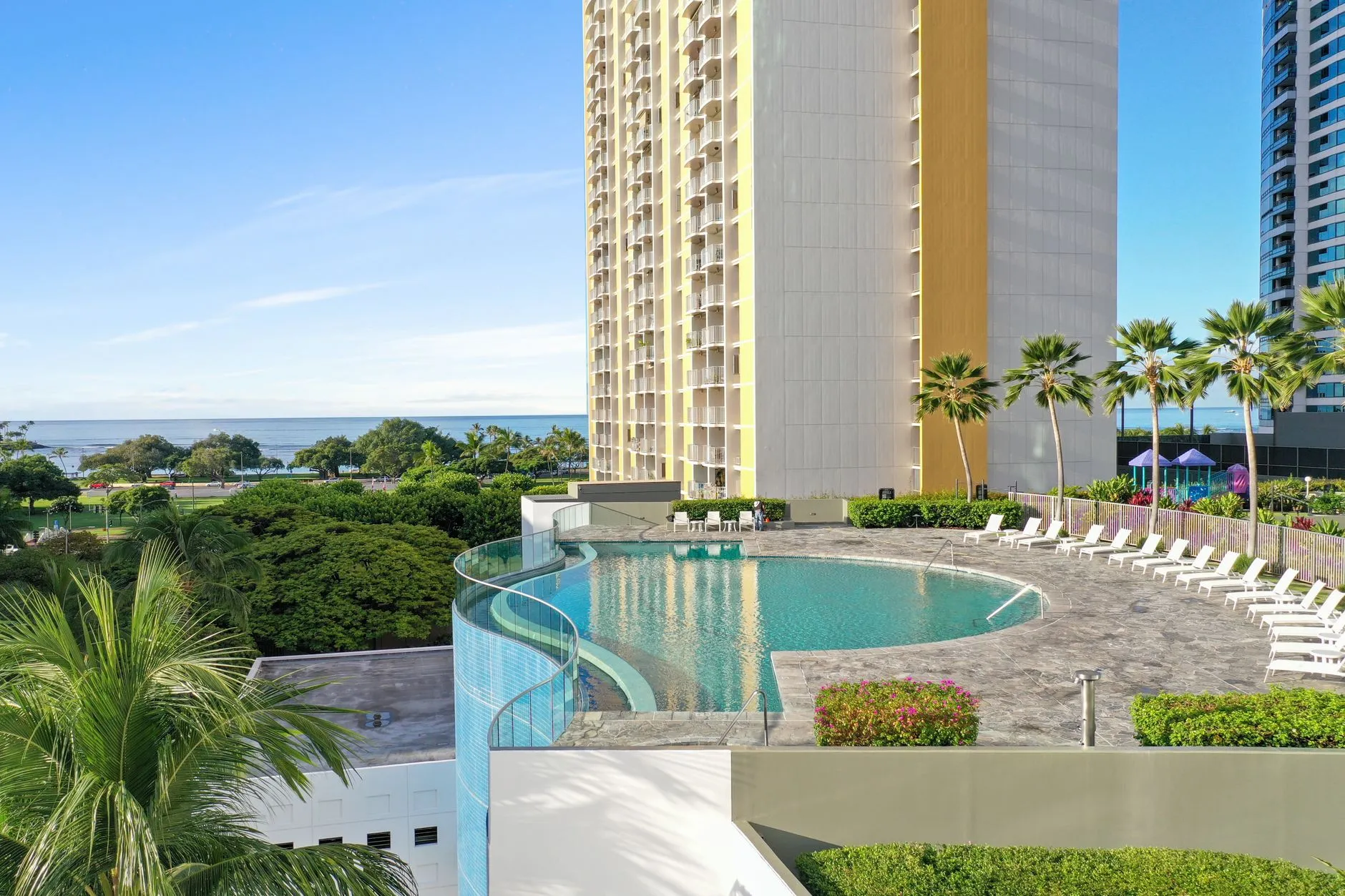 a curved pool deck beside a tower with palm trees and the ocean beyond