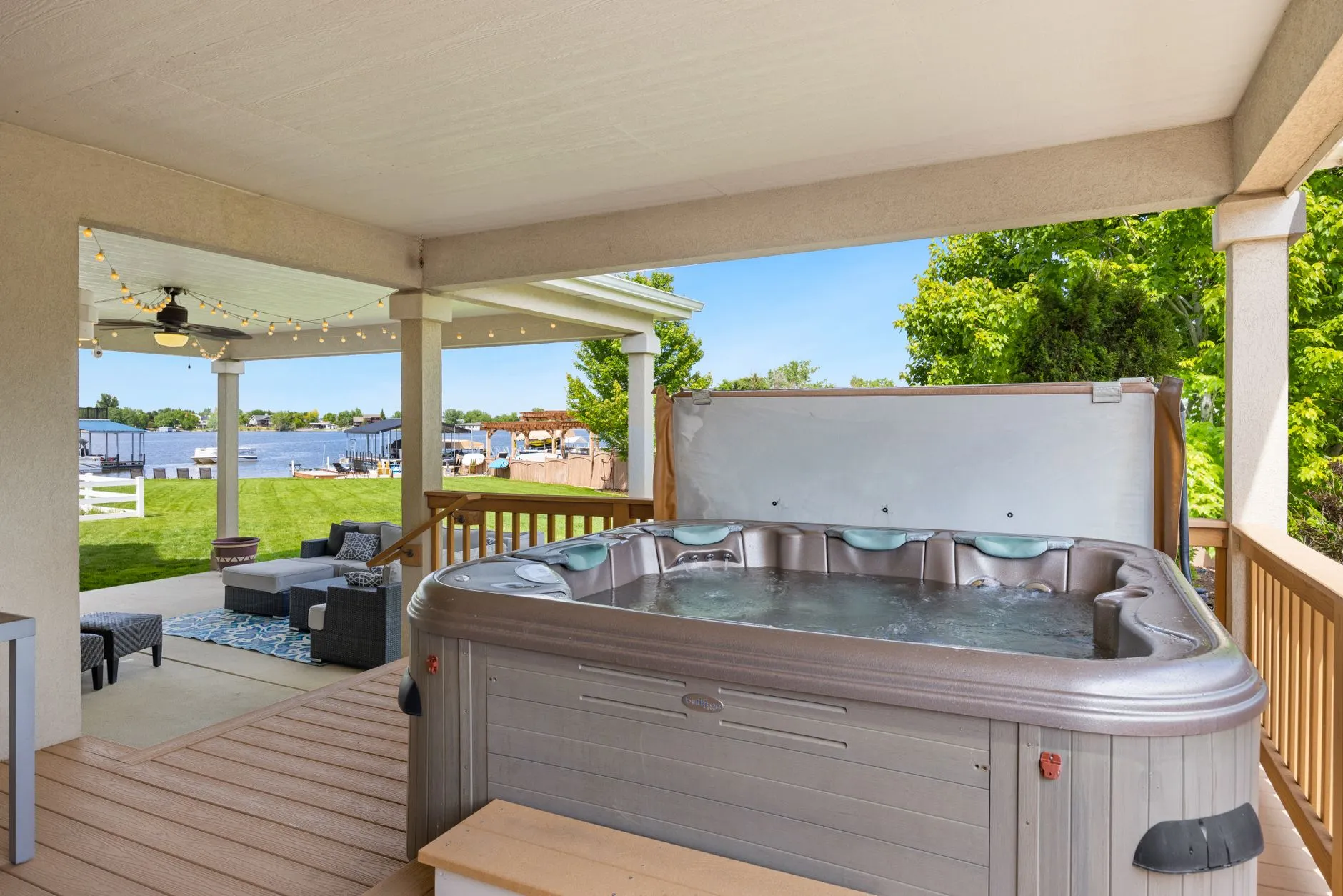 hot tub on a covered patio with a lawn and a lake beyond