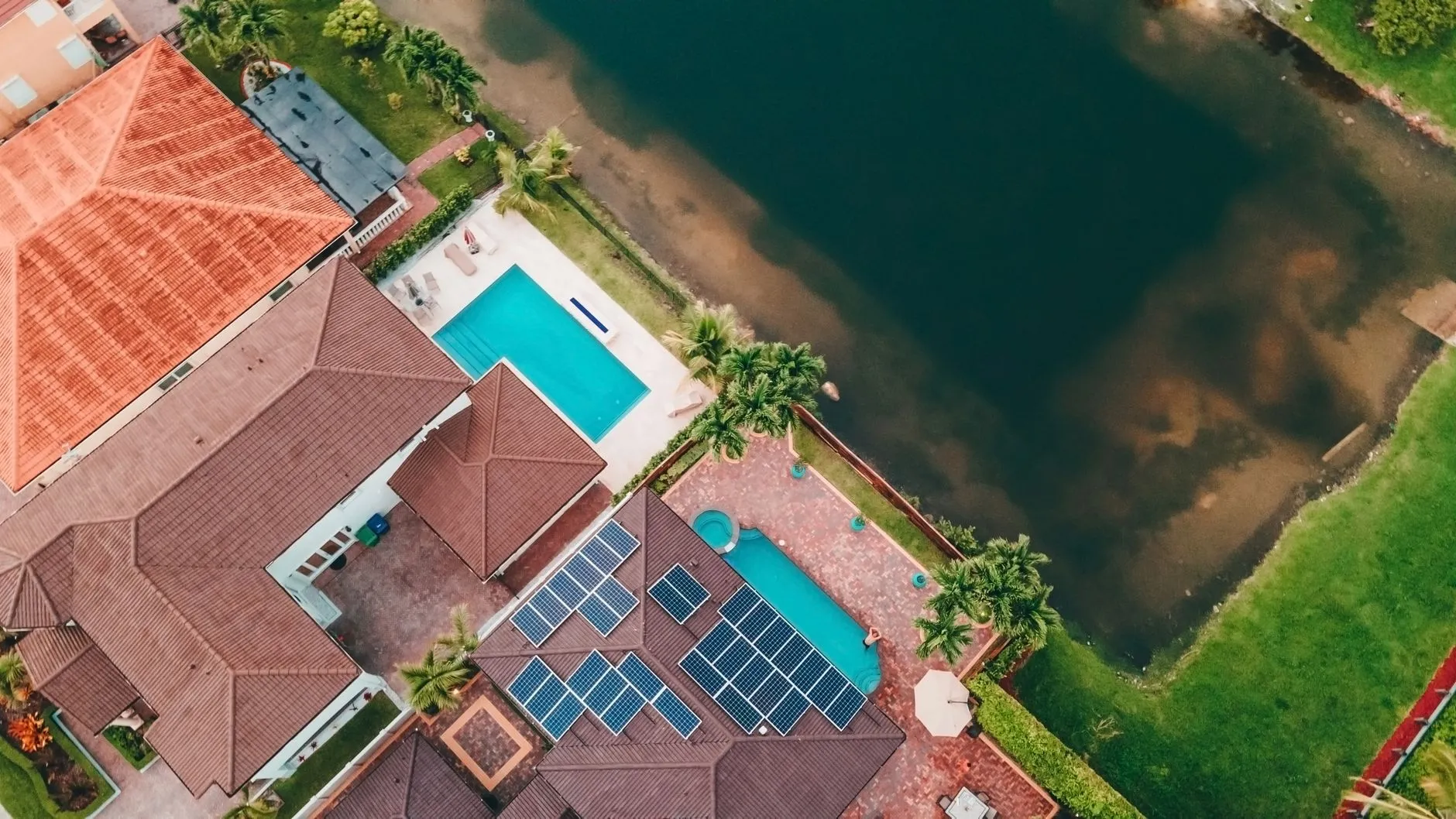 aerial view of tile-roofed waterfront homes with backyard pools and rooftop solar panels