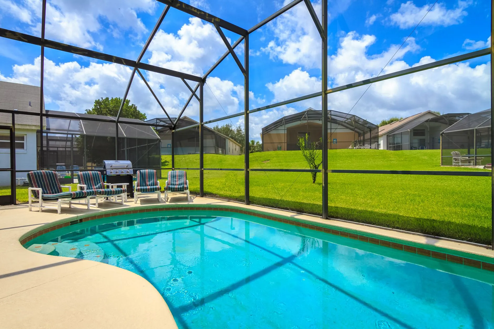 screened backyard pool with lounge chairs and a lawn beyond the cage
