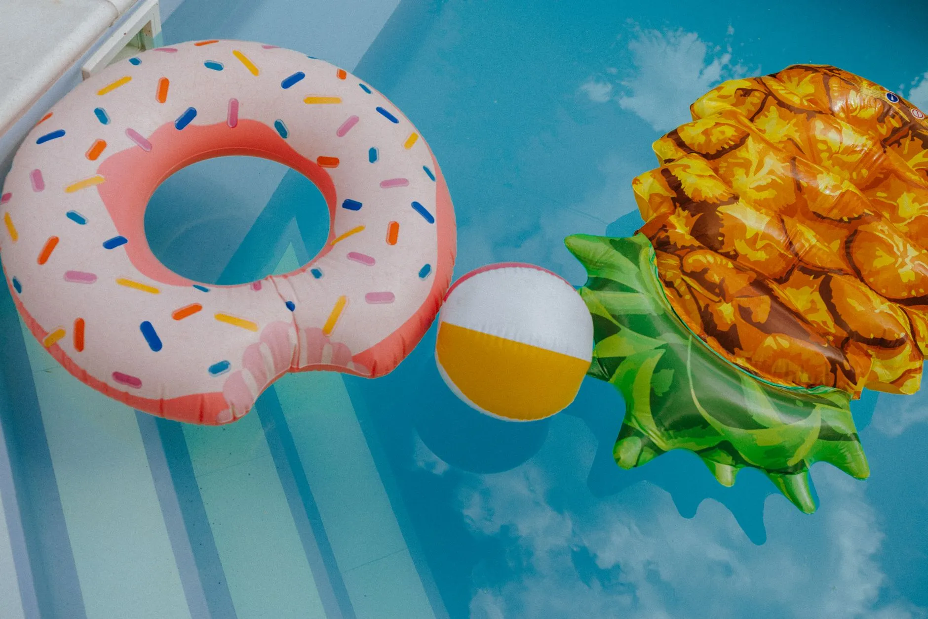 donut and pineapple floats and a beach ball on clear pool water