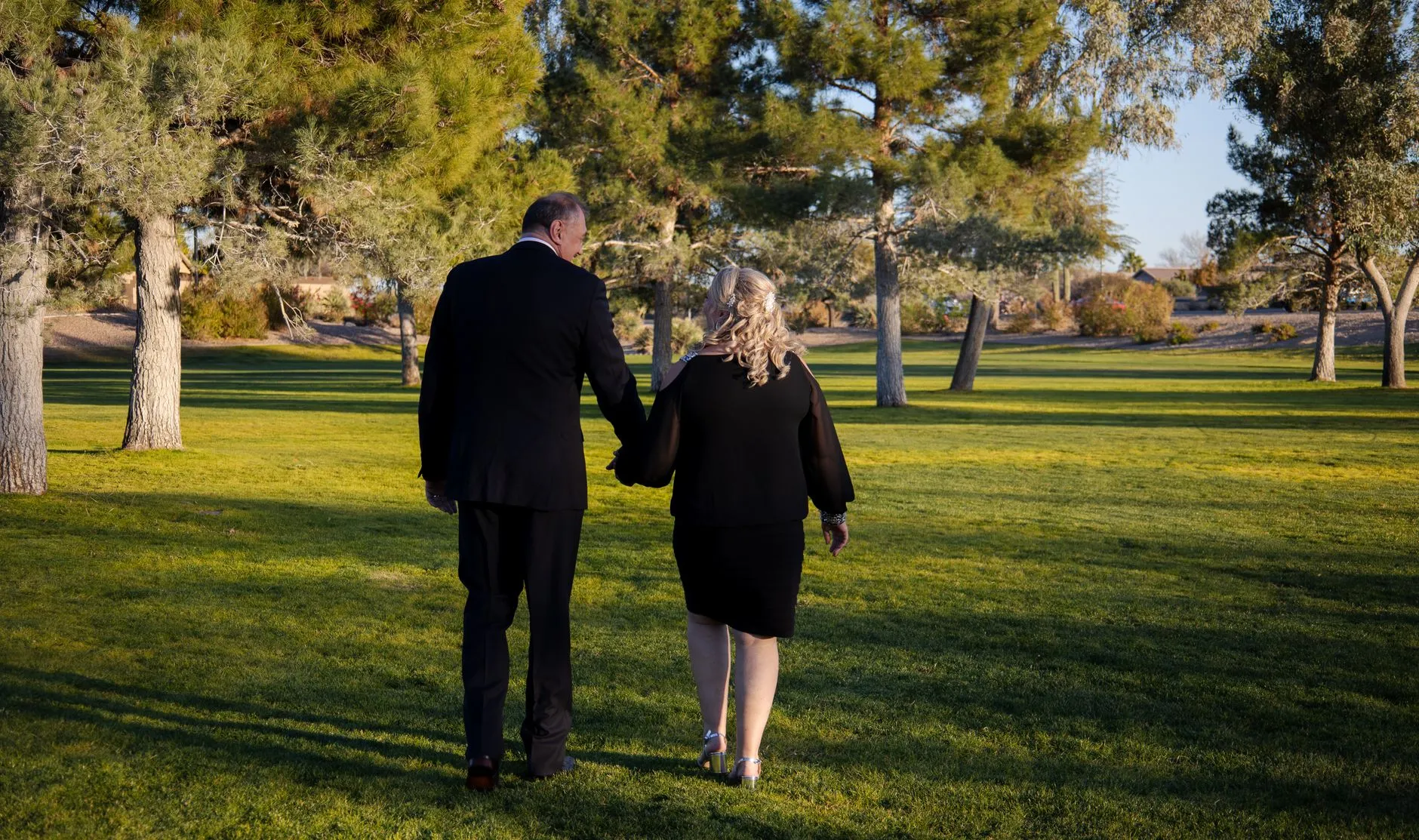 an older couple walking away together across a sunlit lawn