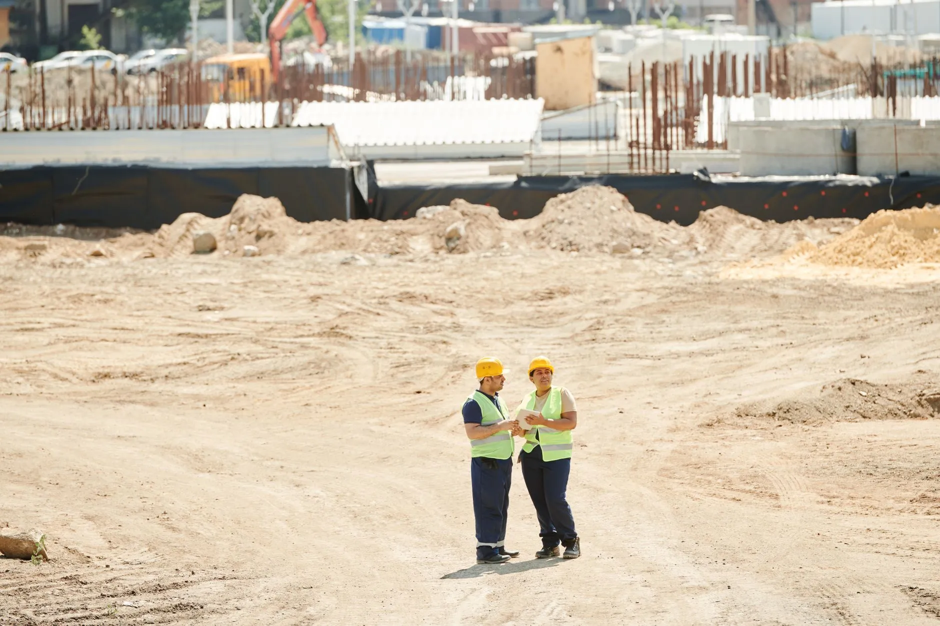 two workers in hard hats and safety vests talking on a cleared construction site