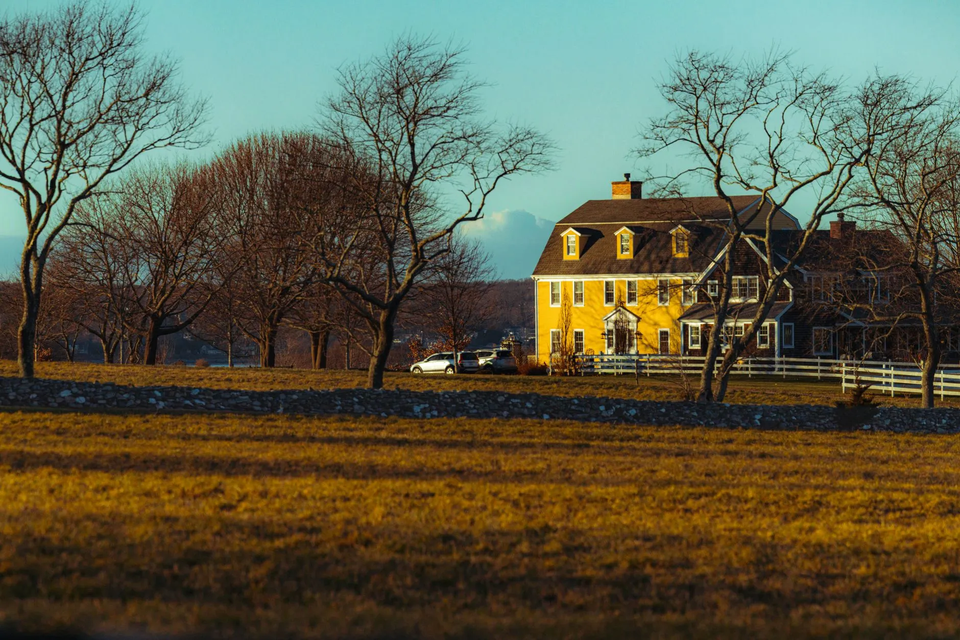 a yellow colonial farmhouse among bare trees in late-afternoon light