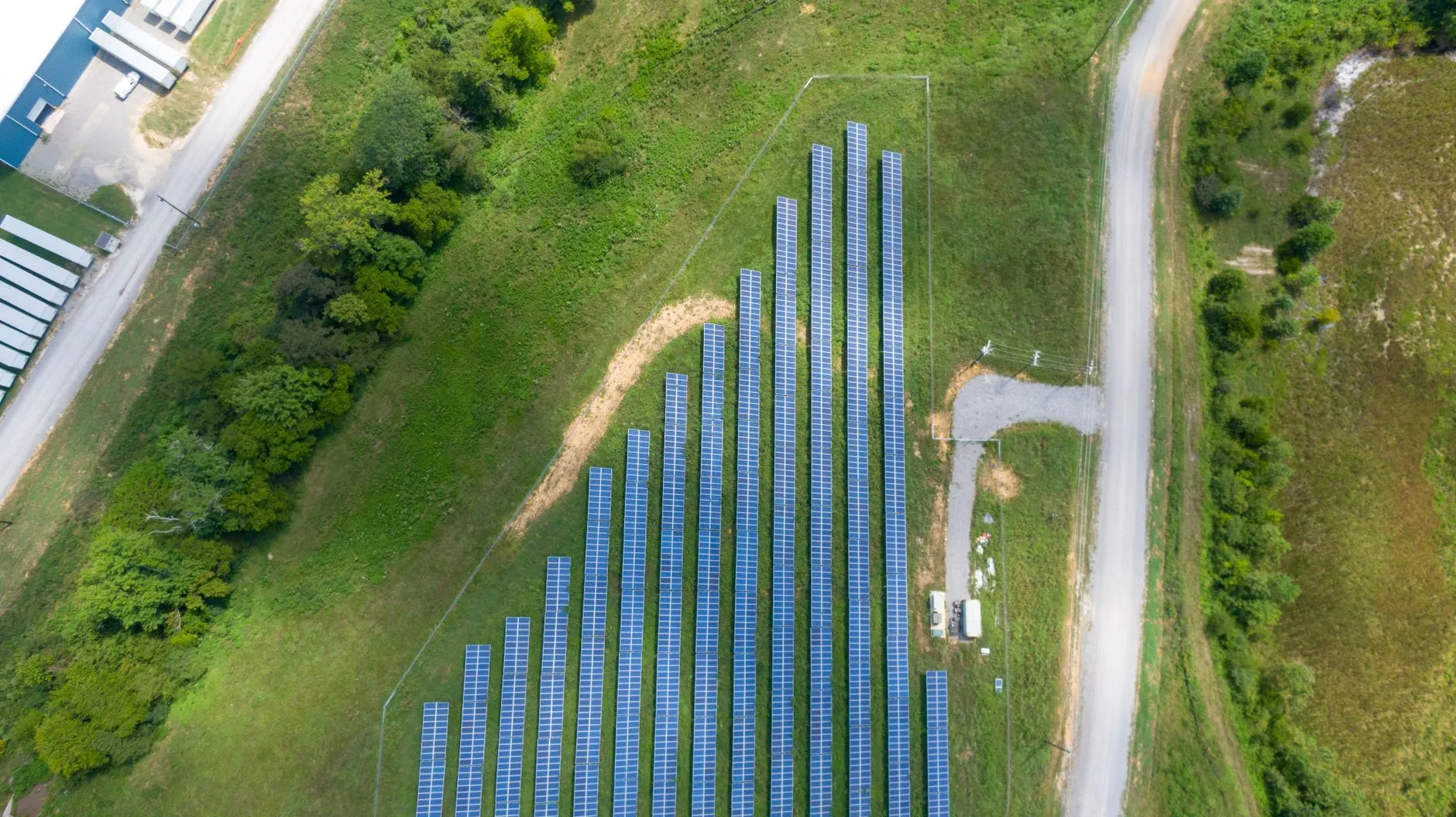 an aerial view of a small solar array on a grassy hillside beside a gravel road