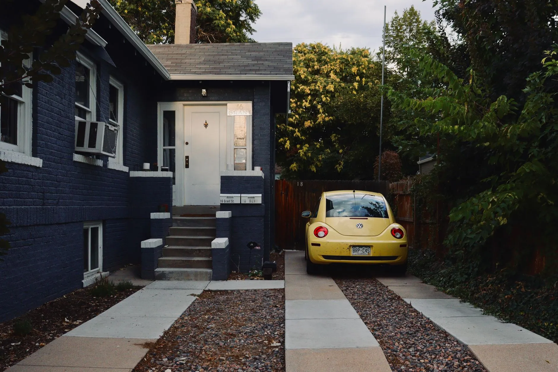 small yellow car parked in a driveway beside a dark blue house