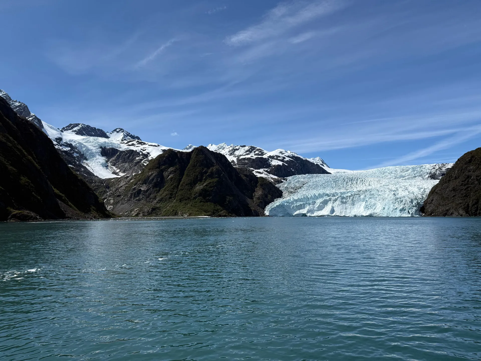 glacier meeting calm water between snowy mountains in an Alaskan fjord