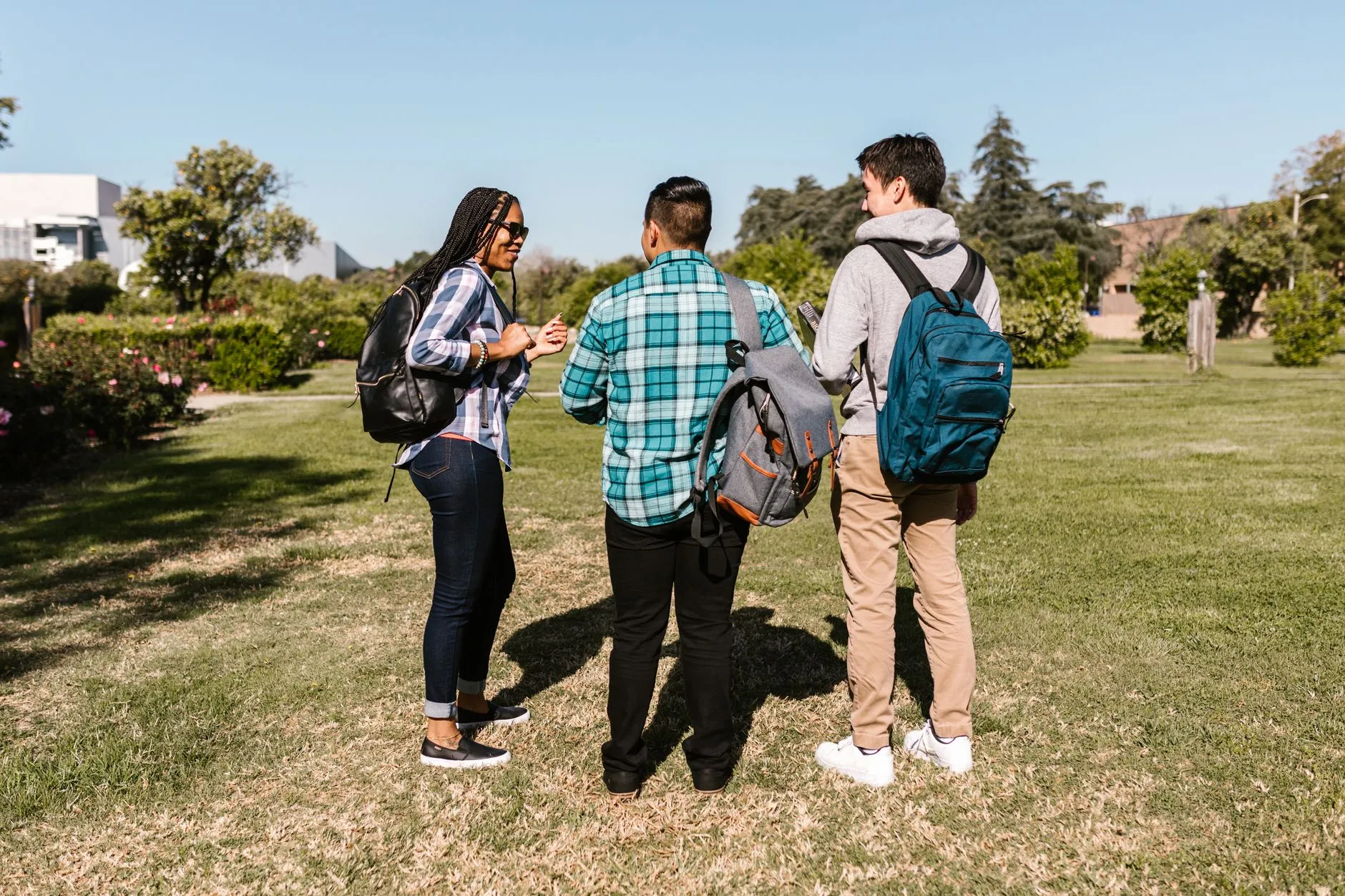 three students with backpacks talking on a college lawn