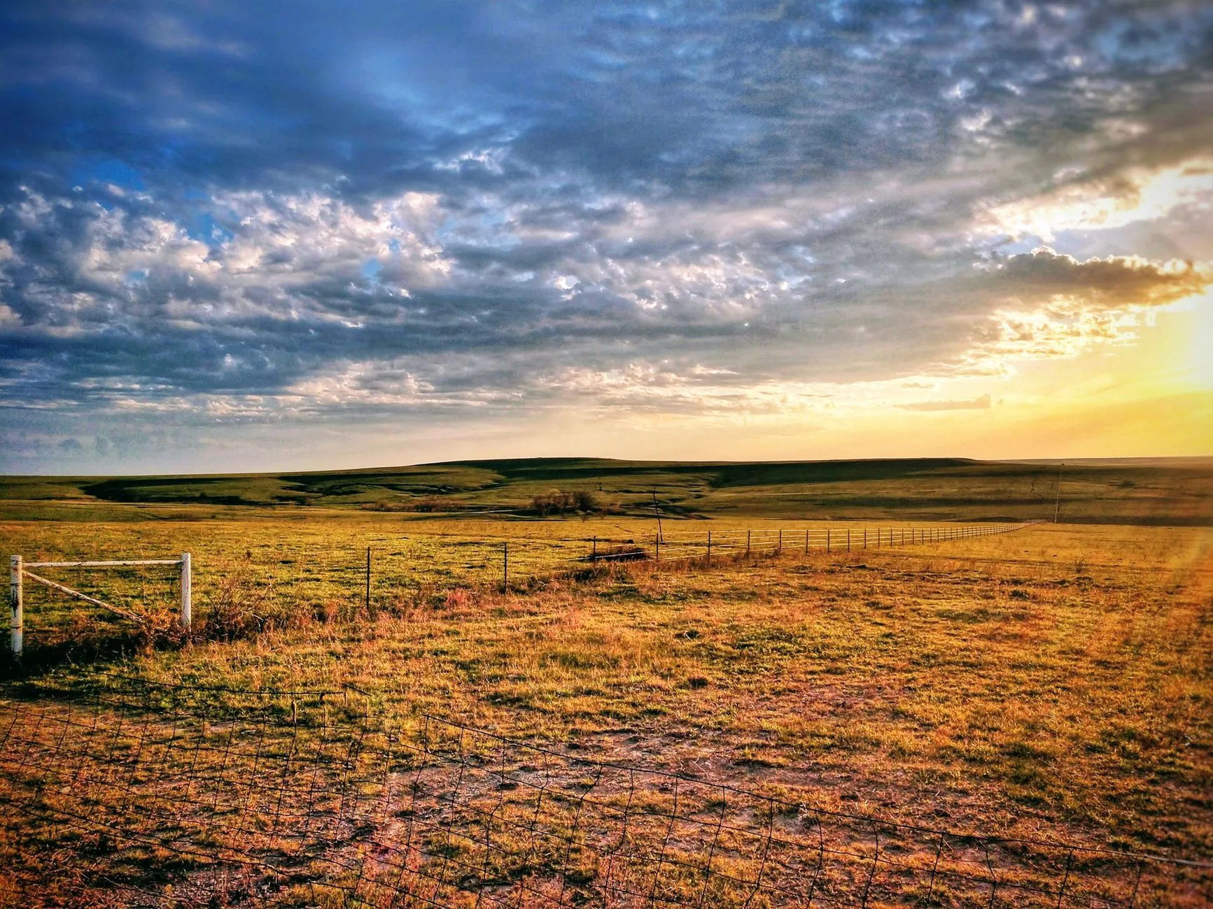 a ranch fence line stretching across the plains at sunset