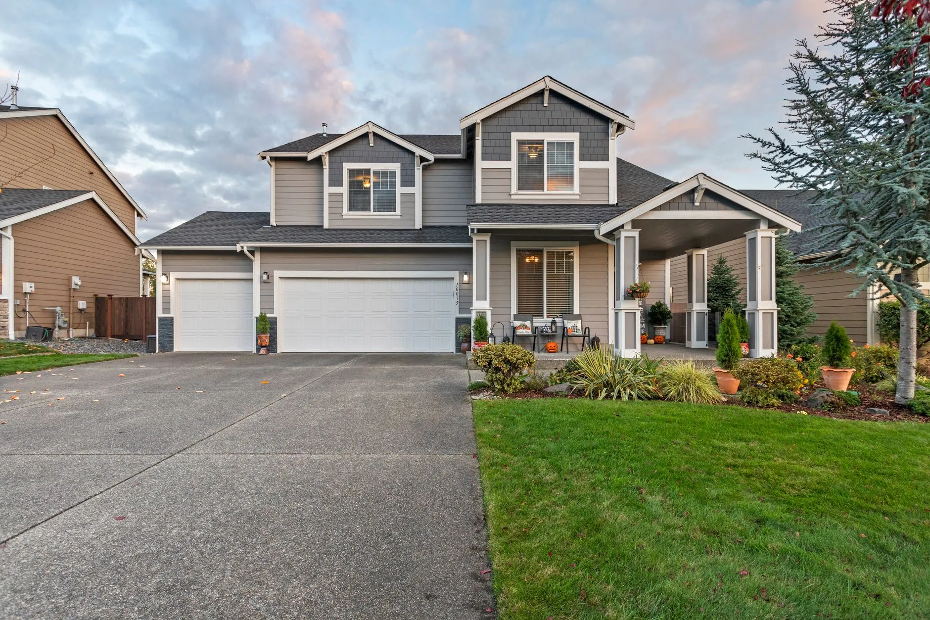 gray two-story house with garage doors and a green lawn