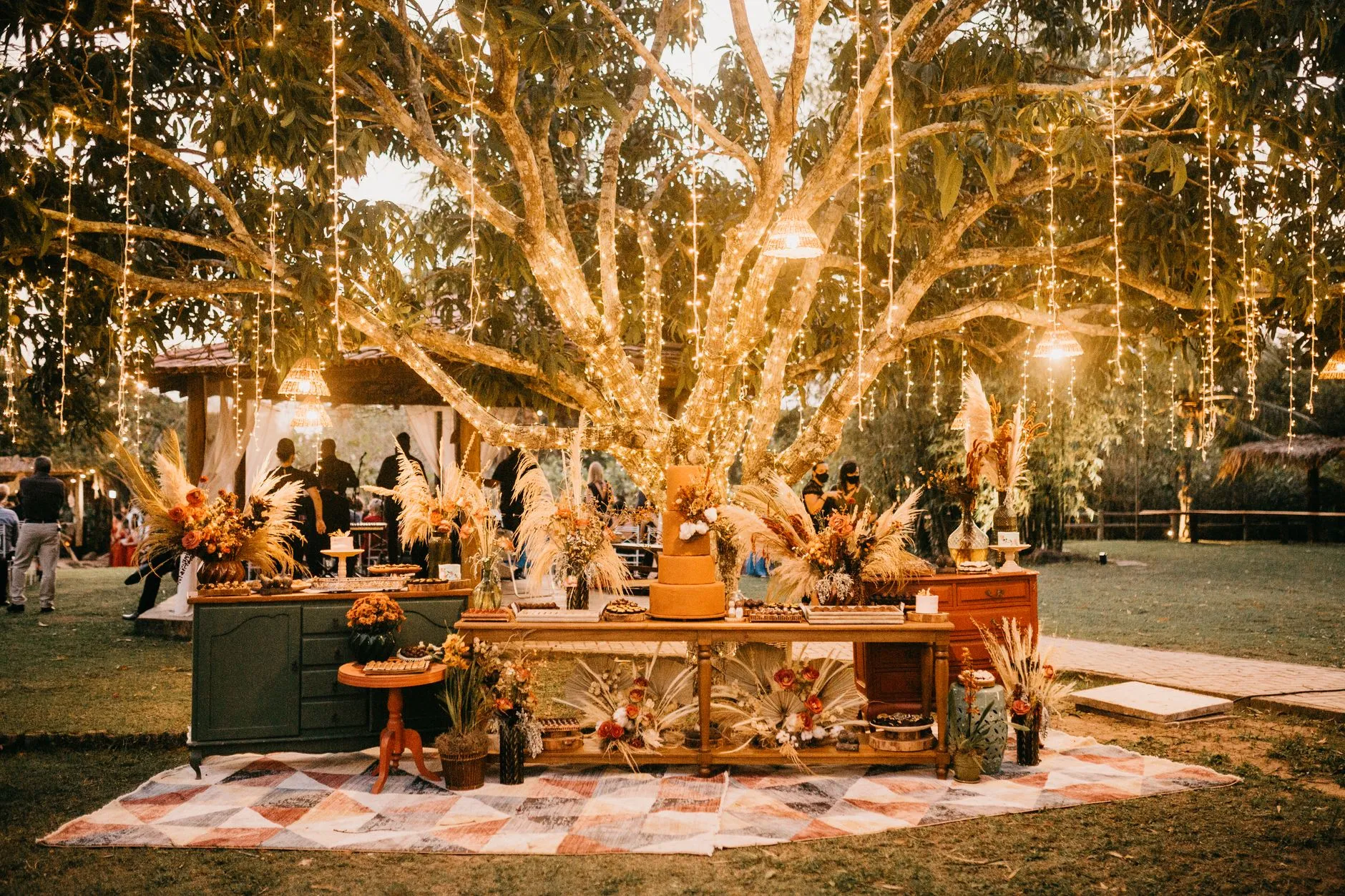 boho outdoor wedding reception with pampas grass and string lights under oak trees