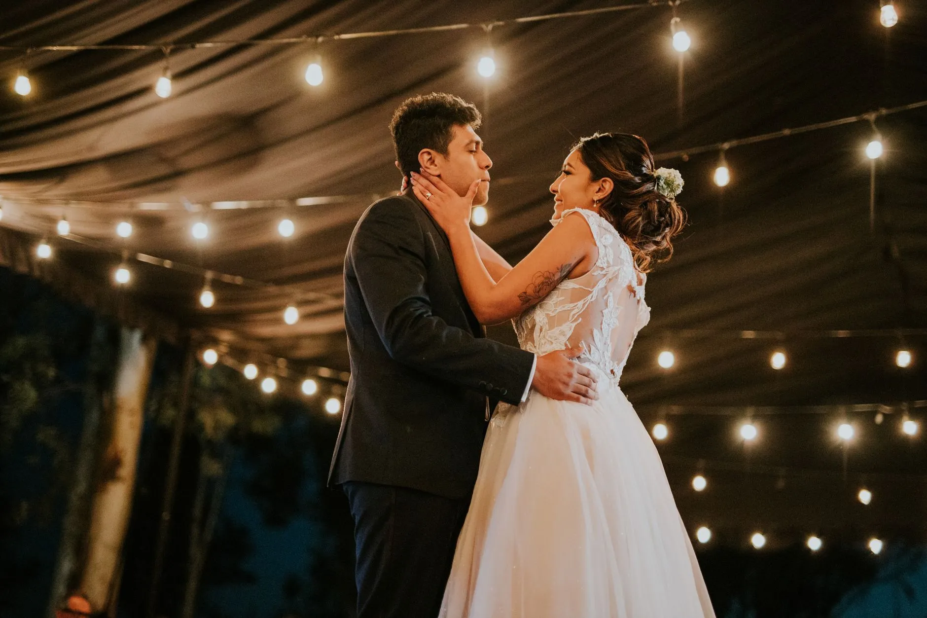 bride and groom first dance under string lights at a reception