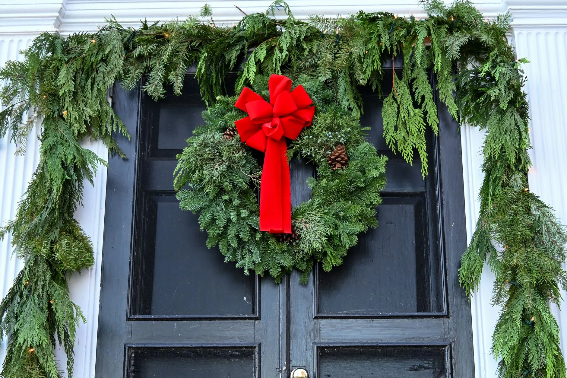 black front door with an evergreen wreath, red bow and garland