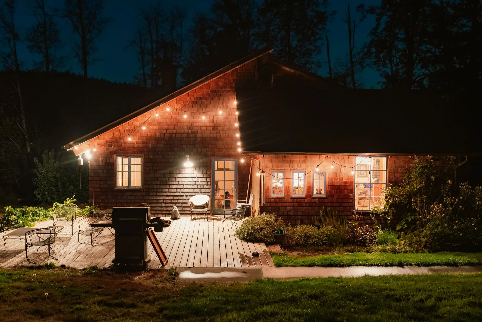 cabin with warm lights along the roofline and a lit deck at night