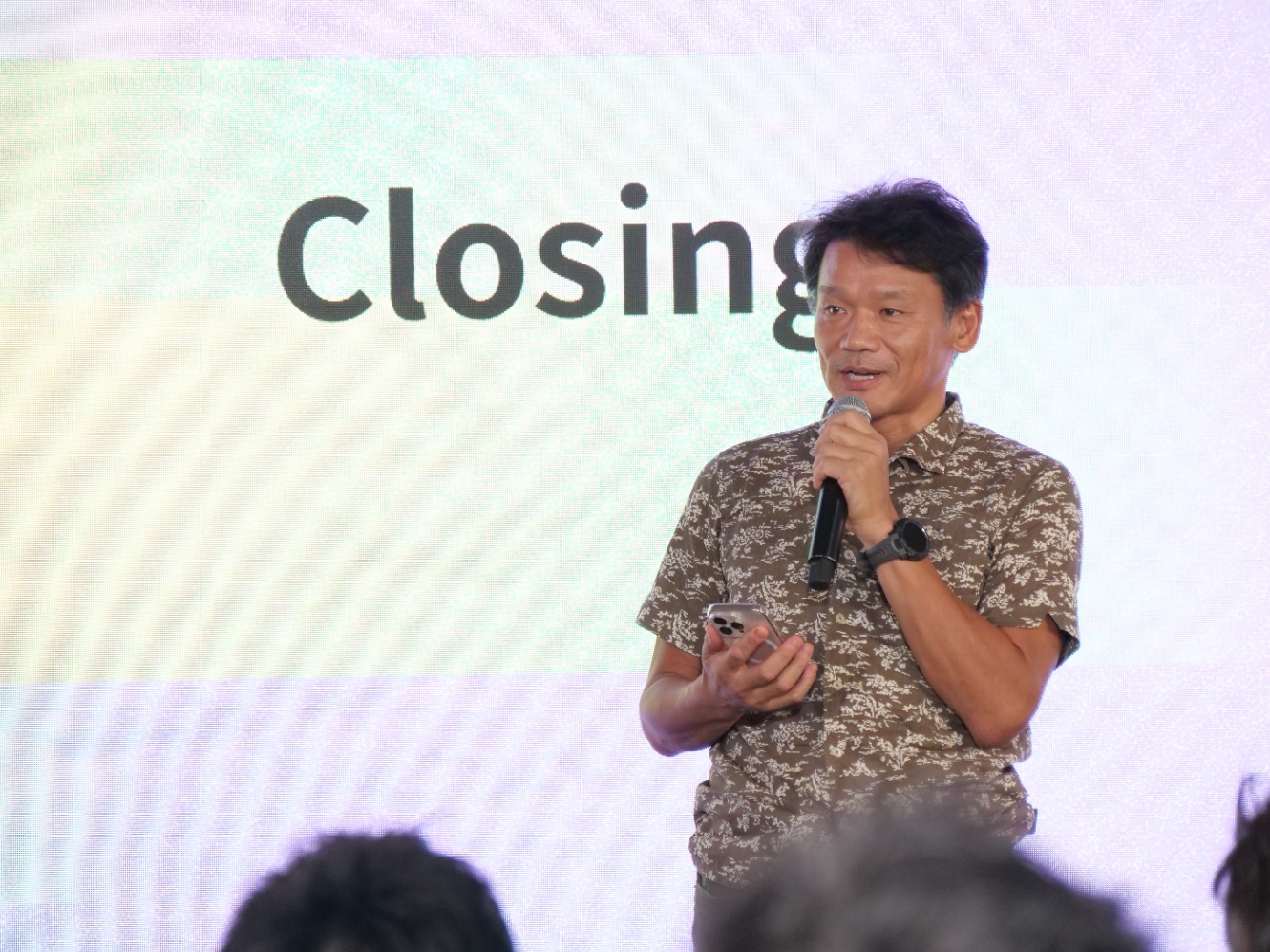 マイクを手にスピーチする宮坂学氏。背景には「Closing」の文字が表示されたスクリーンがある。