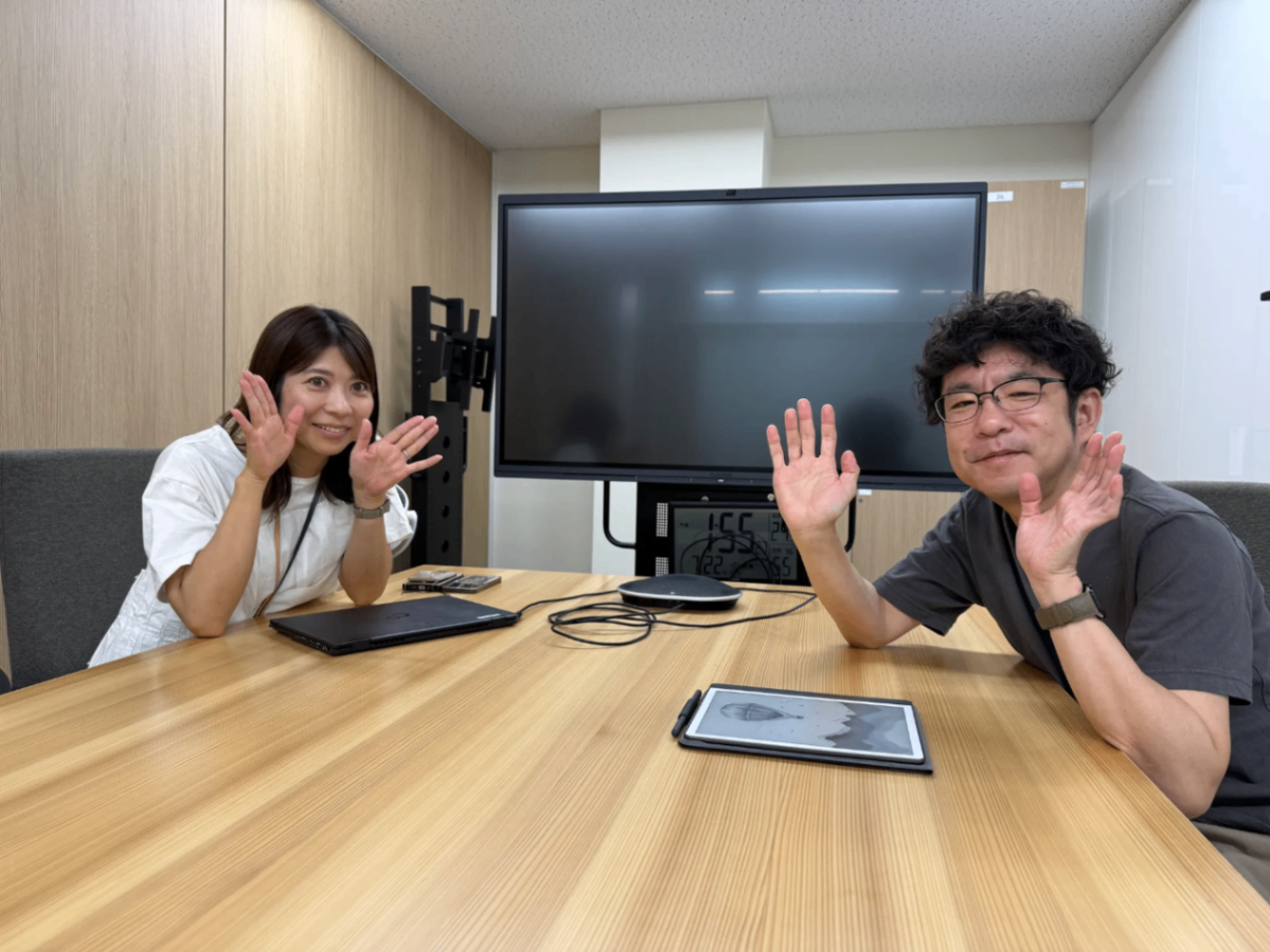 オフィス内の会議室にてこちらを向いて笑顔の2人