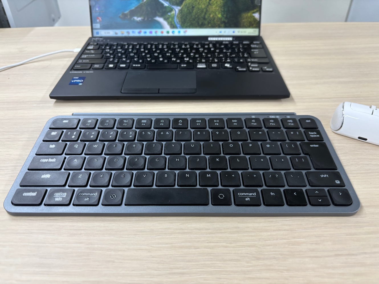 デスクに置かれた薄型キーボードの奥に、黒いノートPCが開いている