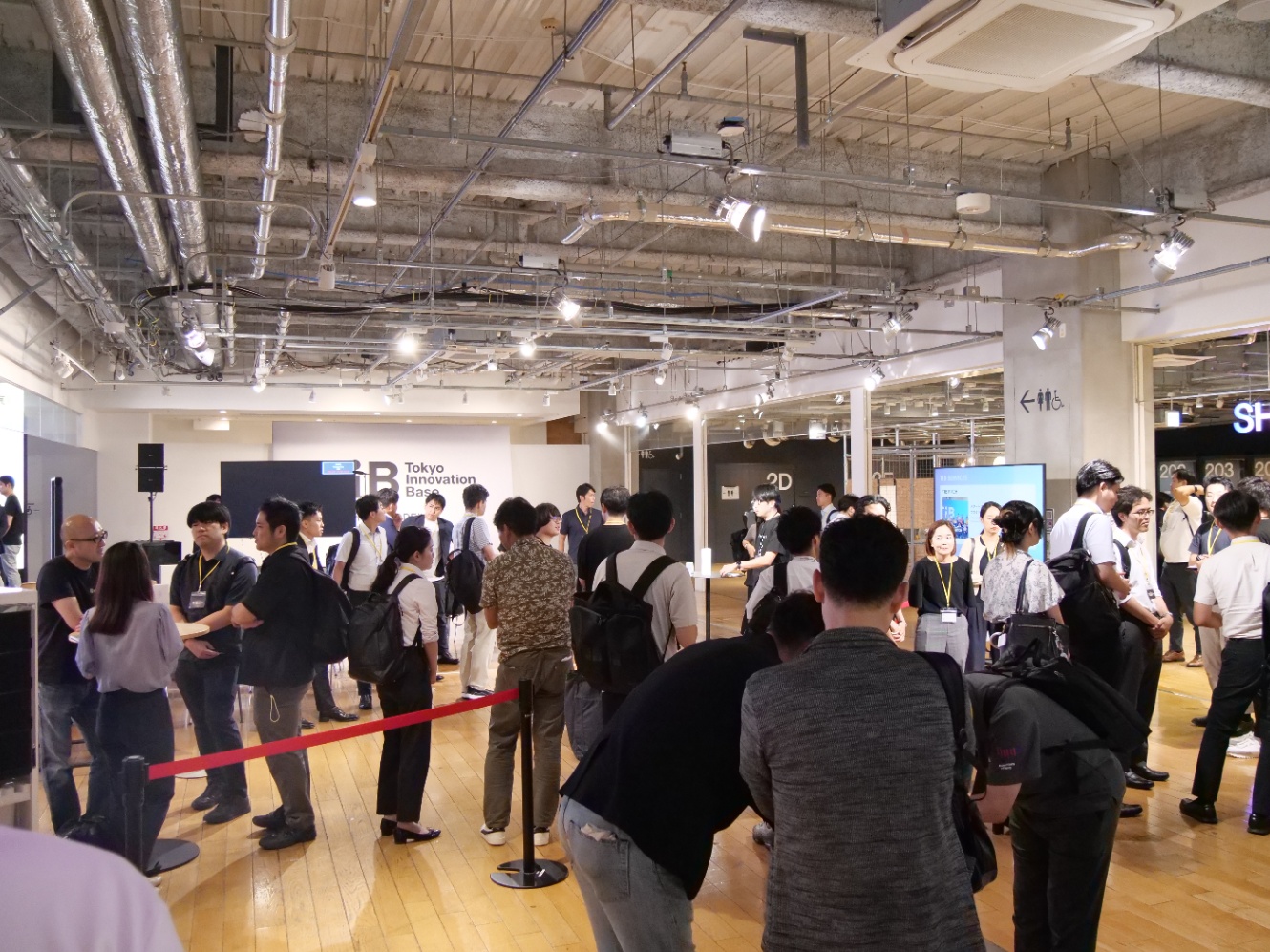 多くの来場者が登壇者ブースに立ち寄りし、会話を交わしている様子。天井には配管や照明がむき出しで、インダストリアルな雰囲気。