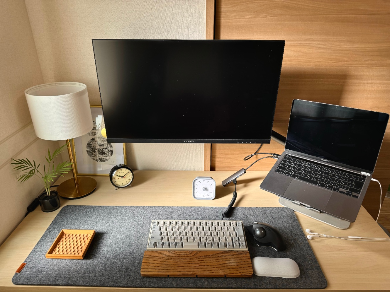 わたしのデスクの写真です。真ん中には27インチのモニターをモニターアームで吊るし、右にはMacBook Pro、フェルトのデスクマットの上にキーボードやマウスなどを置いています。不要なものを極力減らして、モニターに集中できるようにしています。